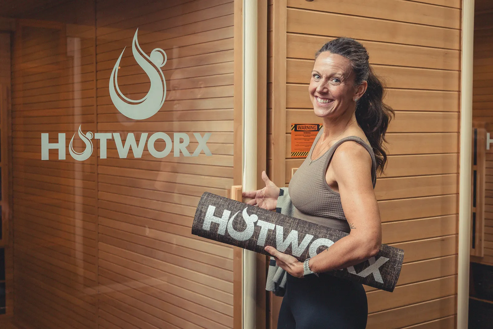 Smiling woman holds HOTWORX mat by studio door