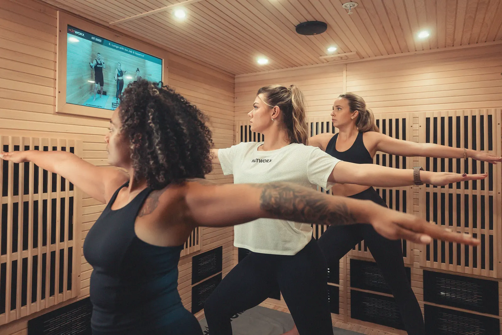 Three women doing yoga in a HotWorx infrared sauna