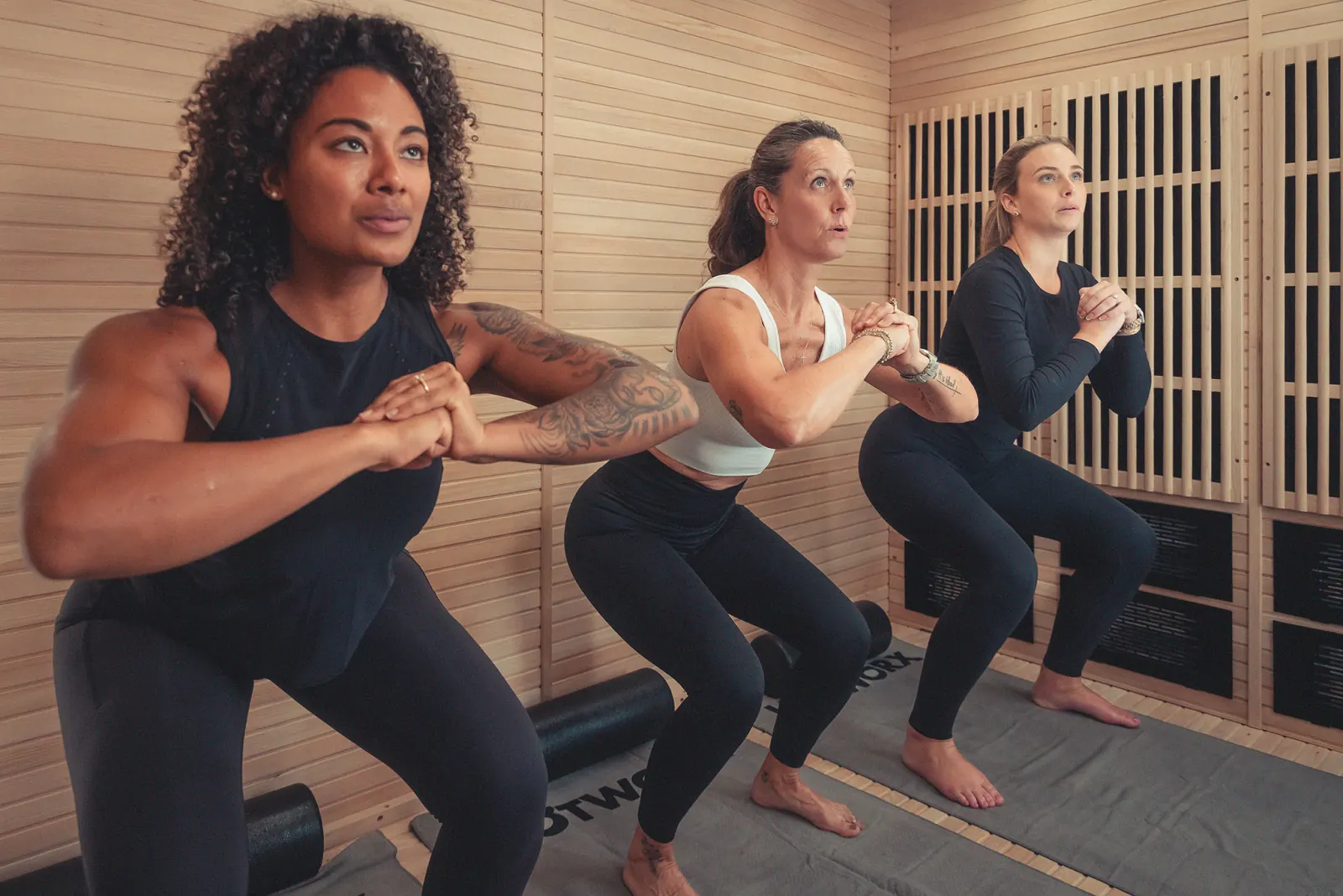 Three women performing squats in a heated studio