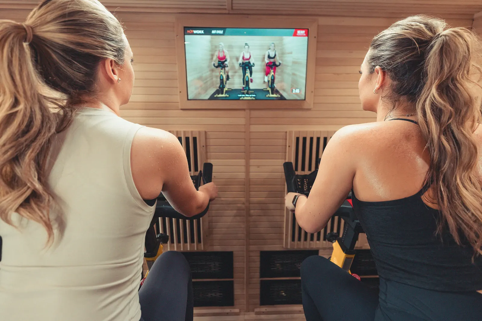 Two women cycling in an infrared sauna following a virtual class.